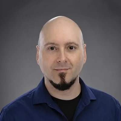 Physical Therapist Jamie Innaco wearing a blue collared shirt and smiling in front of a gray gradient background.
