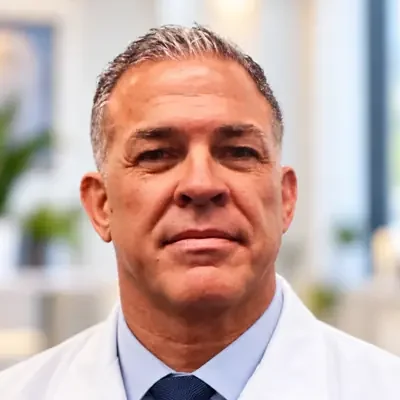 Dr. Ray Marquez smiling in a white coat and tie